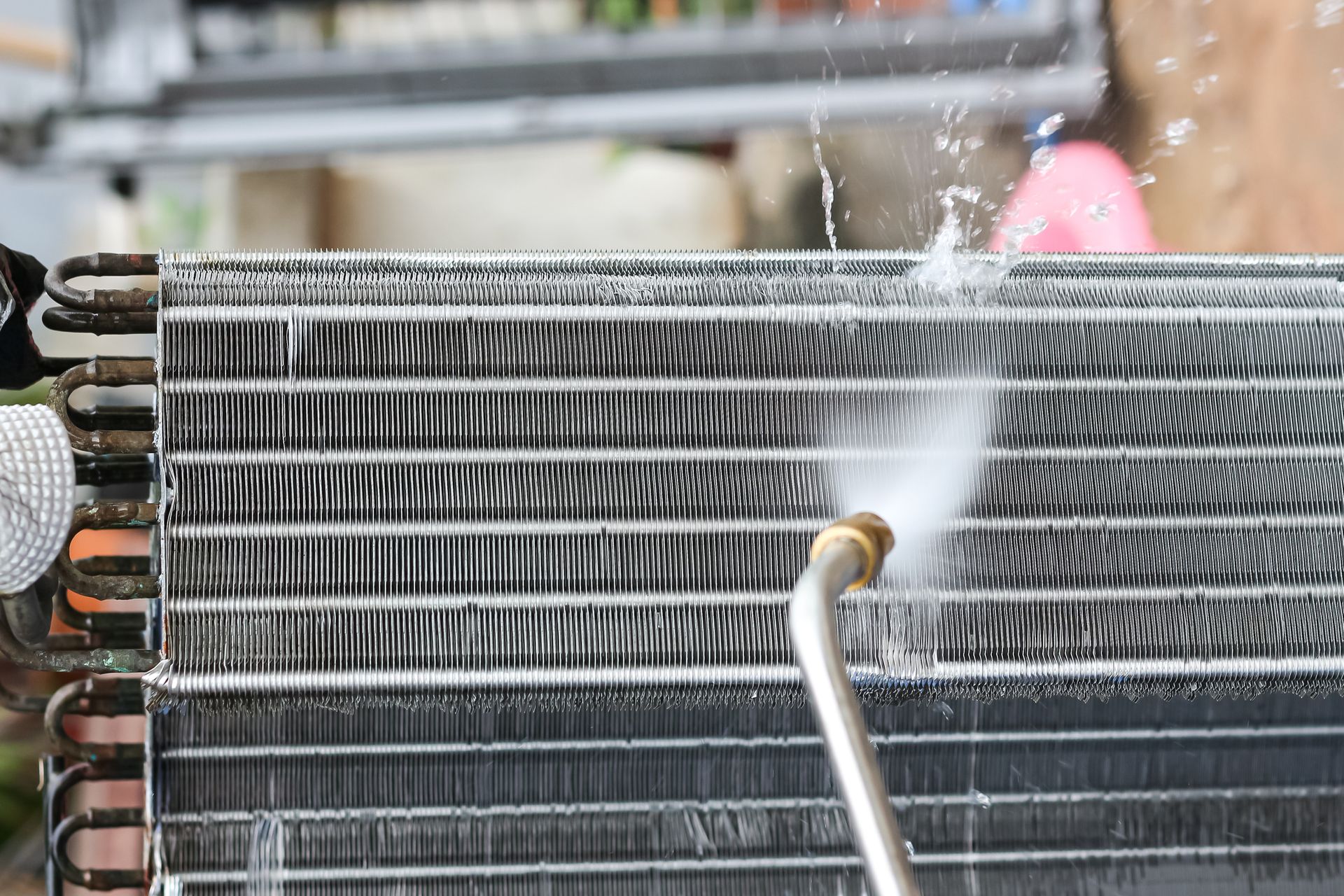 Cleaning spray nozzle rinsing a dusty metal radiator grille with water.