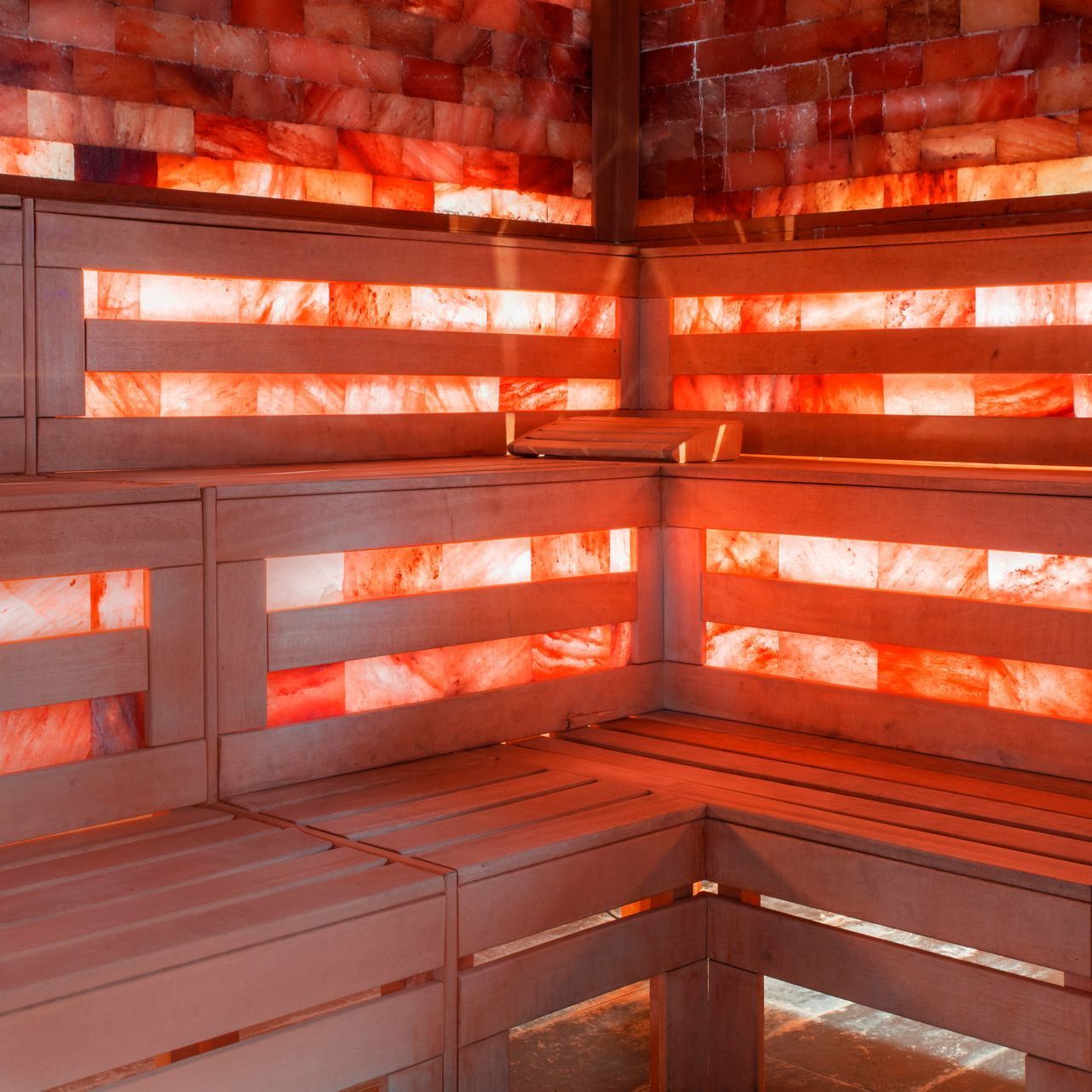 A wooden bench in a sauna with red lights on the walls.