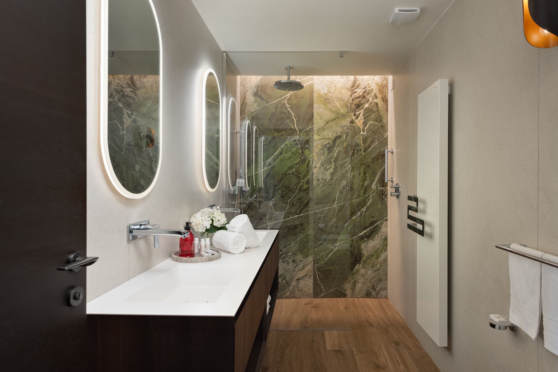 A luxury hotel bathroom with a sink , mirrors , and waterfall shower.