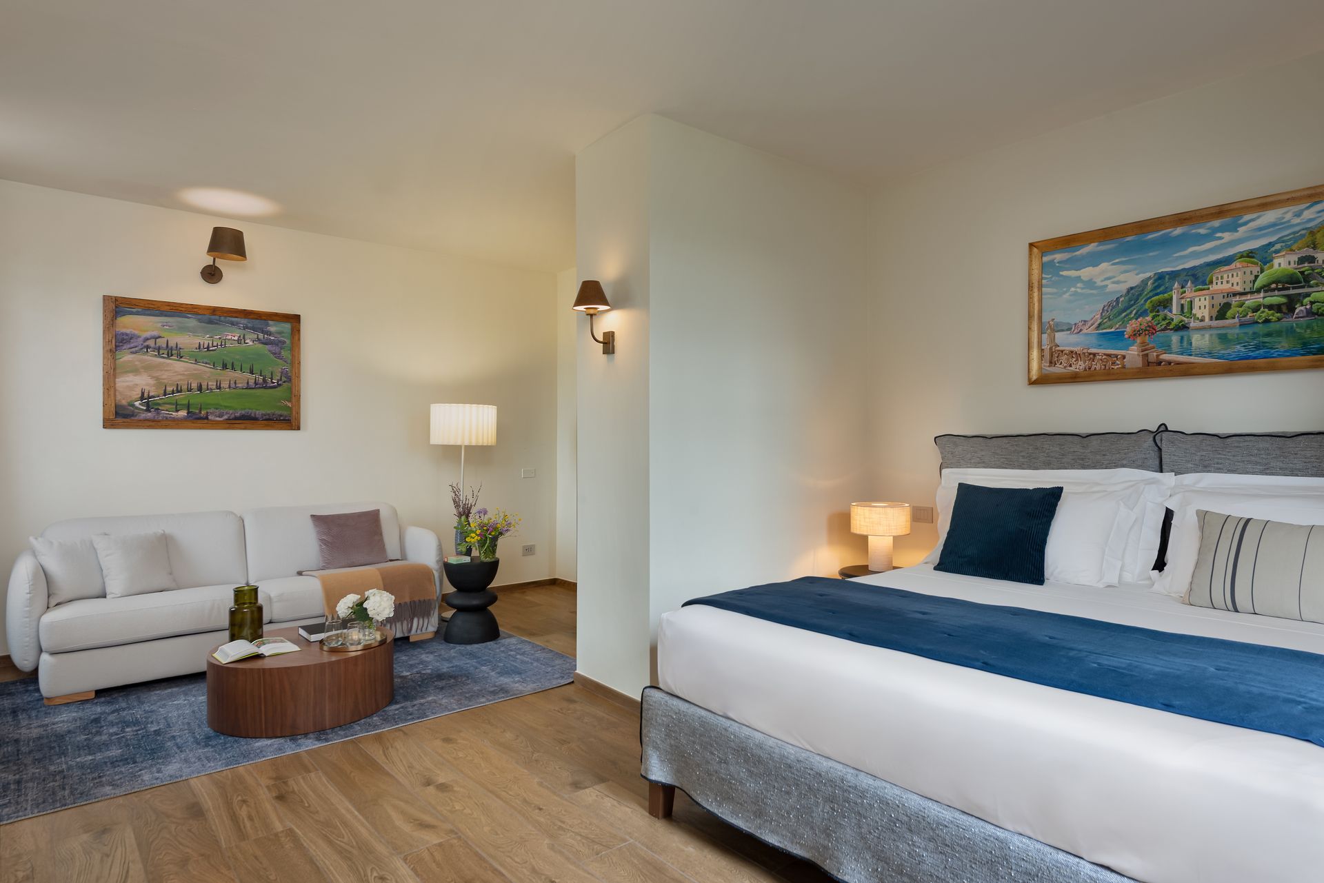 A hotel room with a bed , couch , coffee table and painting on the wall.