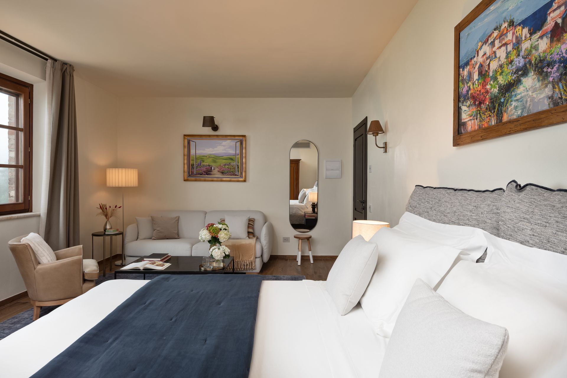 A hotel room with a bed , couch , chair and painting on the wall.