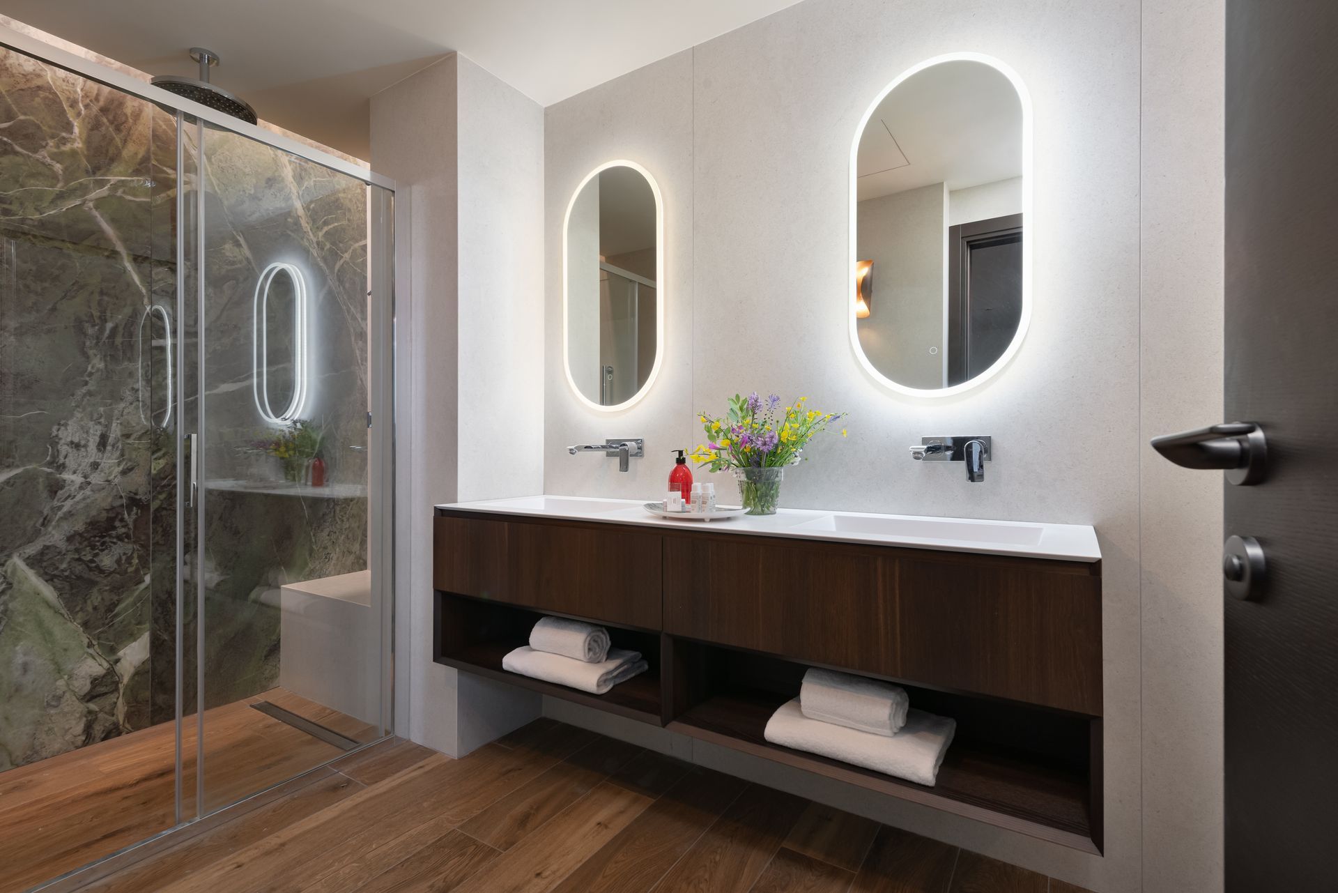 A bathroom with two sinks , two mirrors and a walk in shower.