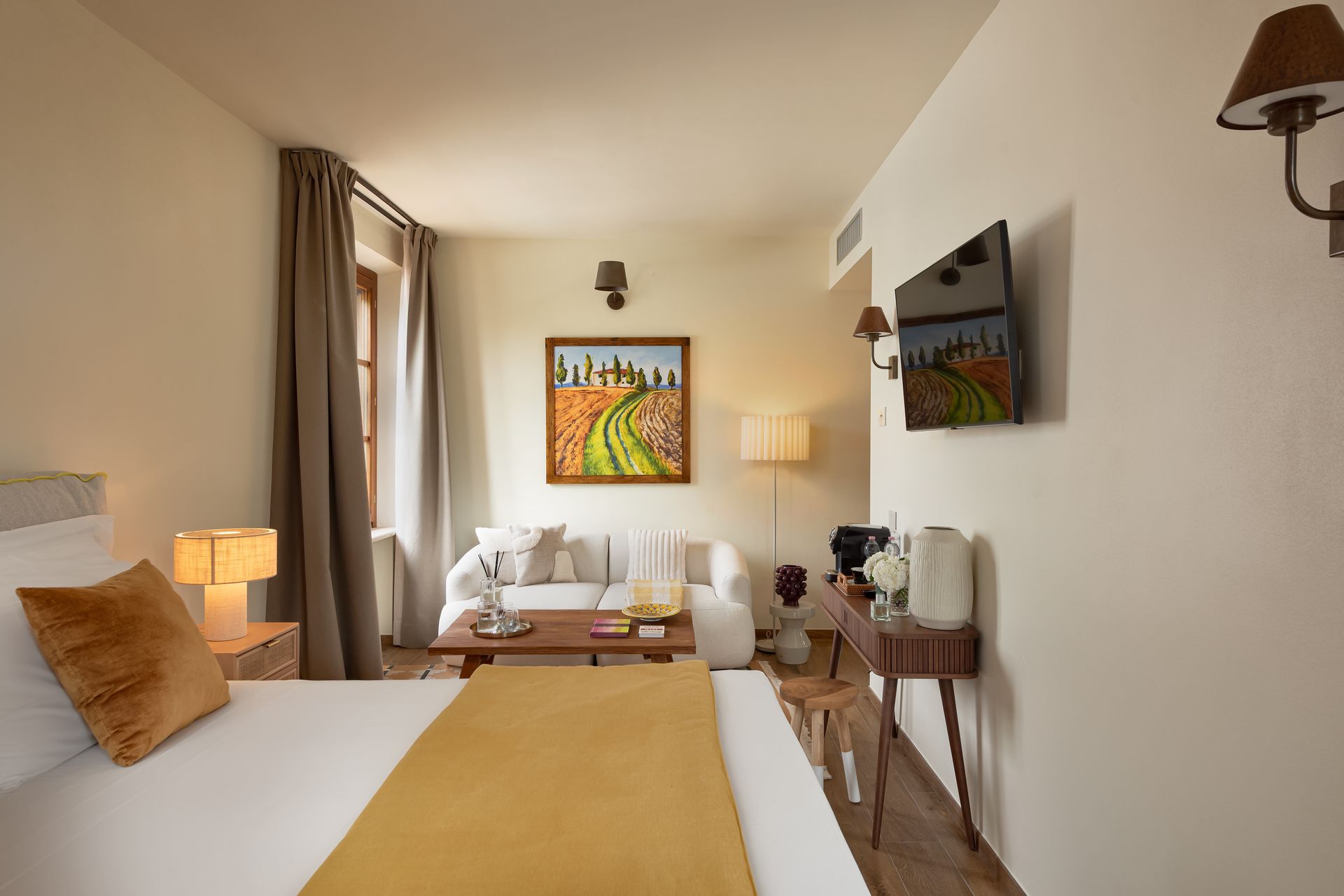 A hotel room with a bed , couch , table , colorful artwork , and television in Tuscany.