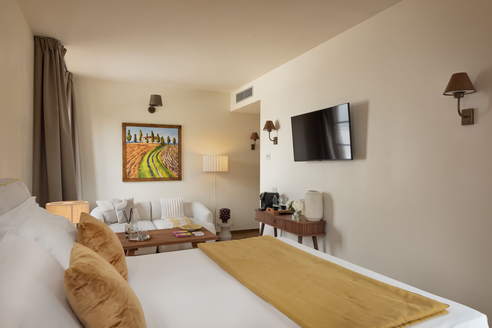A hotel room with a bed , couch , television and painting on the wall in Italy.