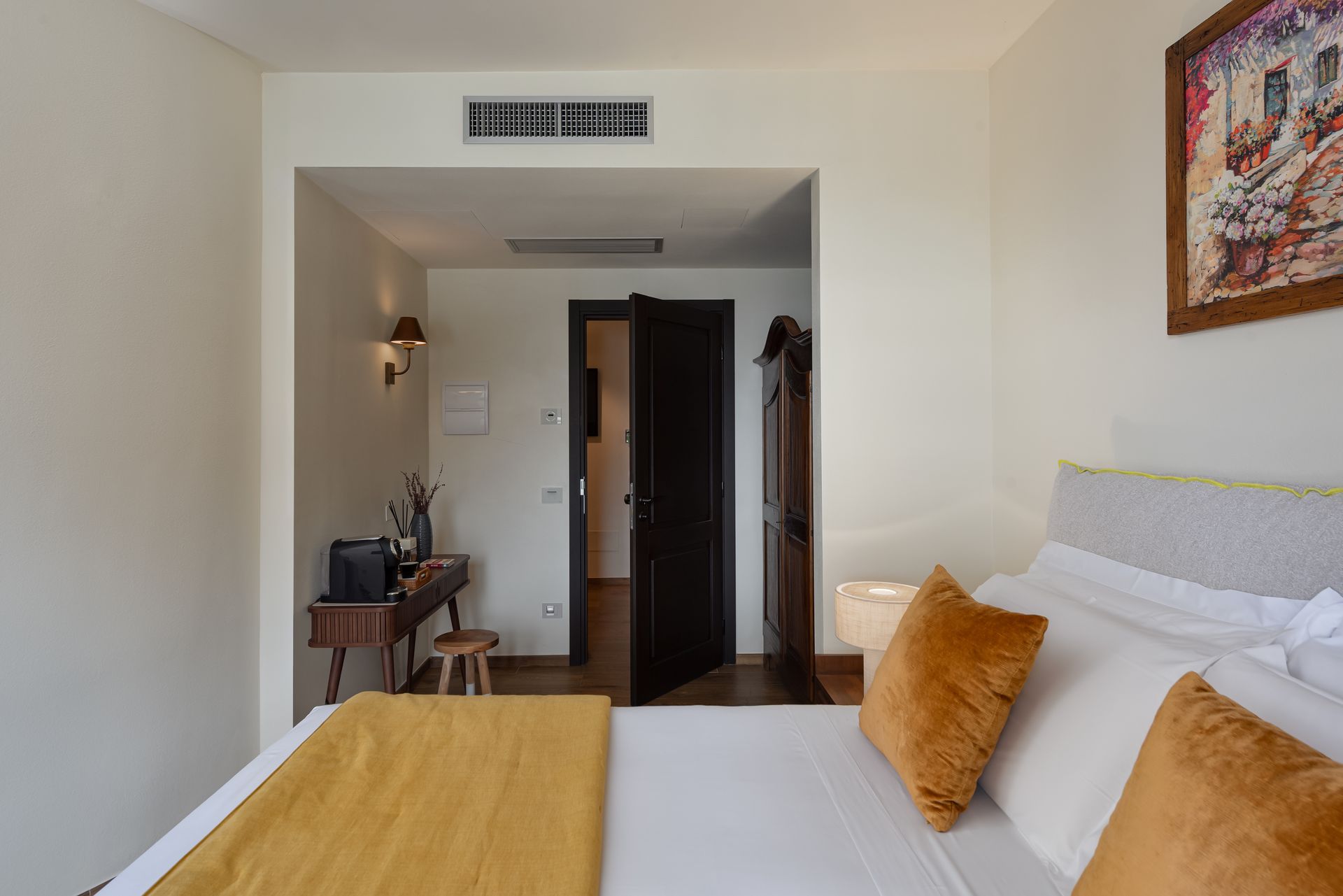 A hotel room with a bed , desk and painting on the wall.