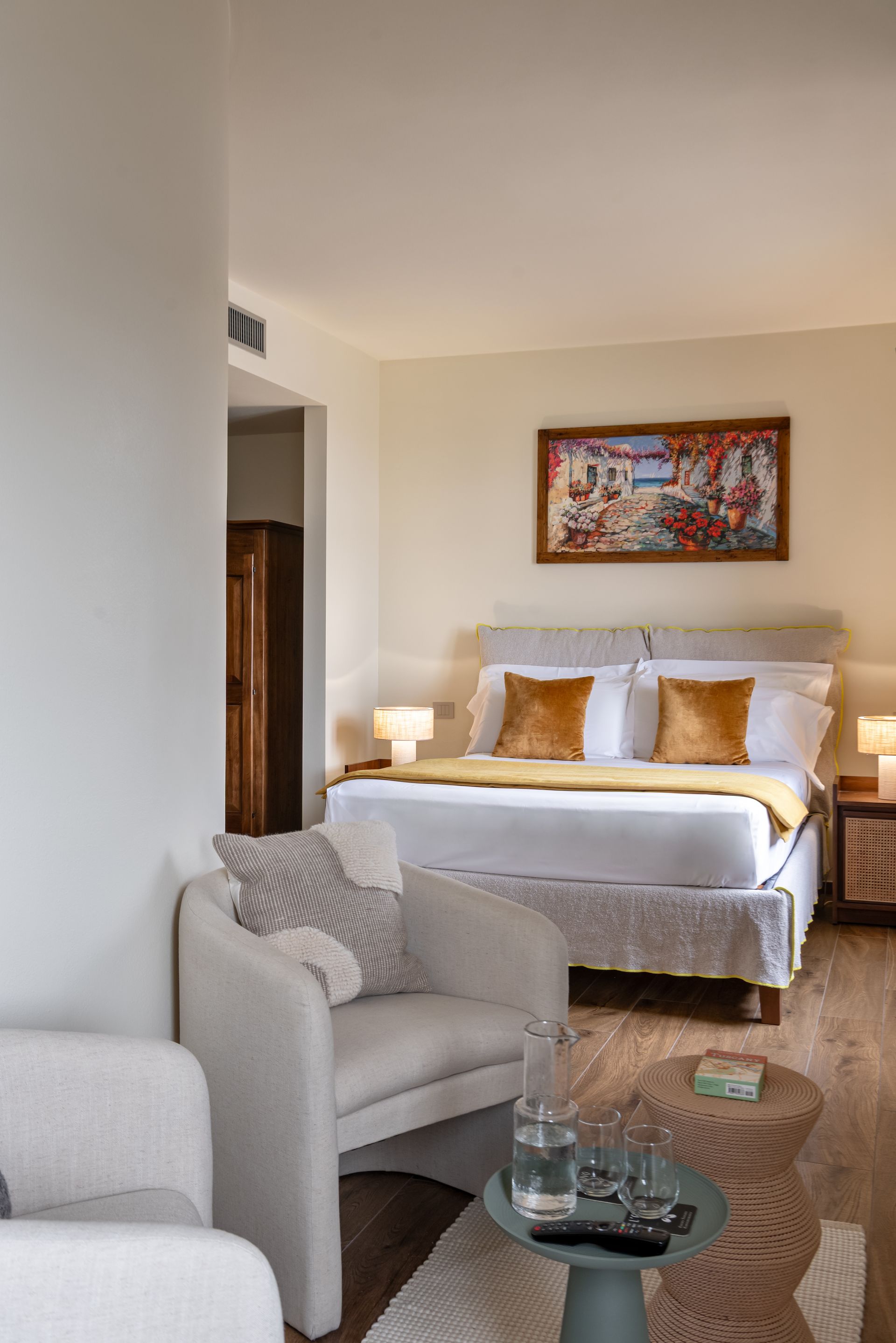 Hotel suite with a king size bed , chair , table and colorful painting on the wall.