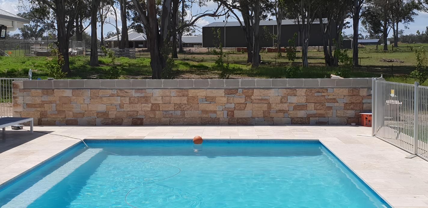 A Large Swimming Pool With A Stone Wall Surrounding It — Lewis Landscapes In Port Macquarie, NSW
