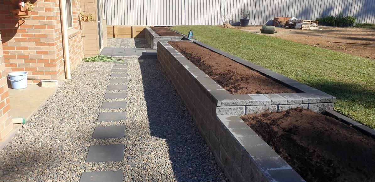 A Stone Walkway Leading To A Brick Wall In A Backyard — Lewis Landscapes In Laurieton