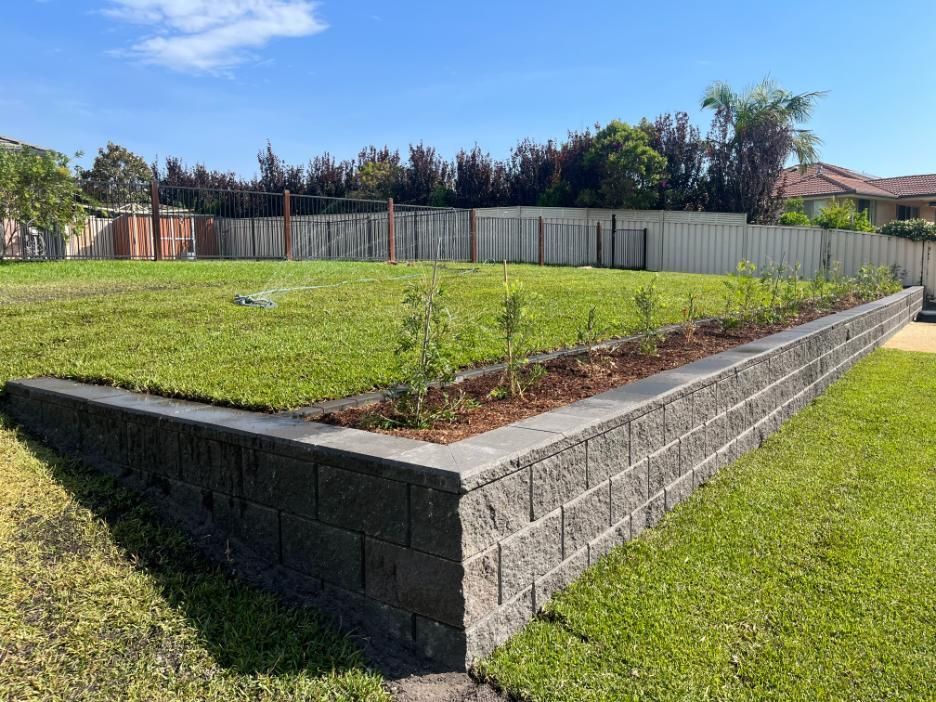 A Brick Wall Surrounds A Lush Green Lawn With A Fence In The Background — Lewis Landscapes In Yippin Creek, NSW