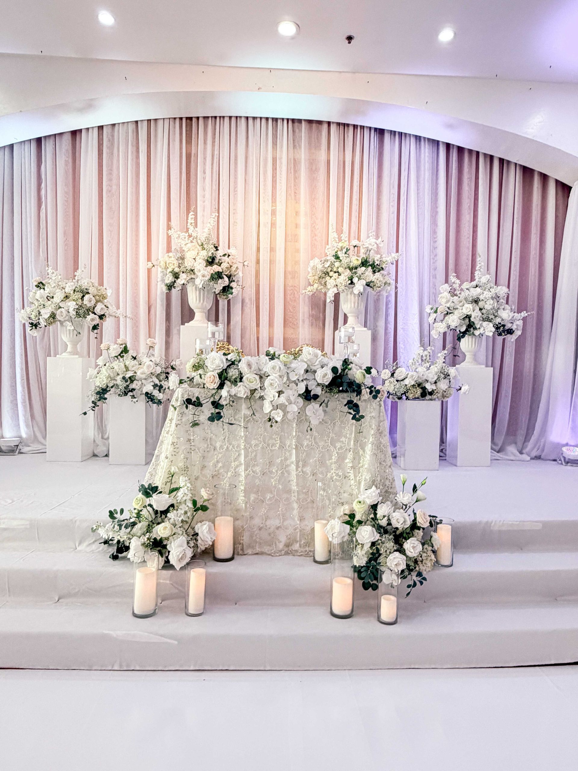 Wedding stage with white floral arrangements and candles.