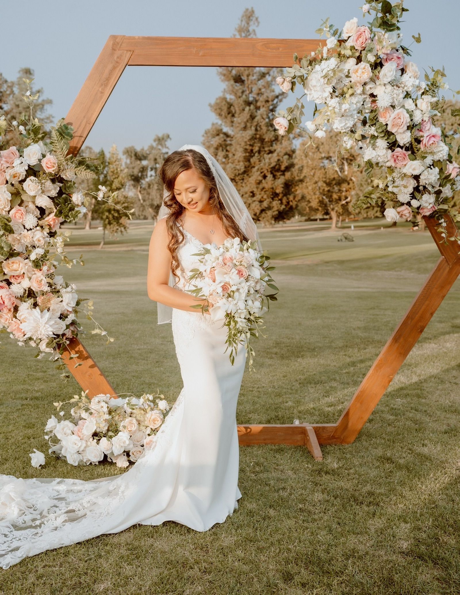 a bride in a white dress stands in front of a floral arch