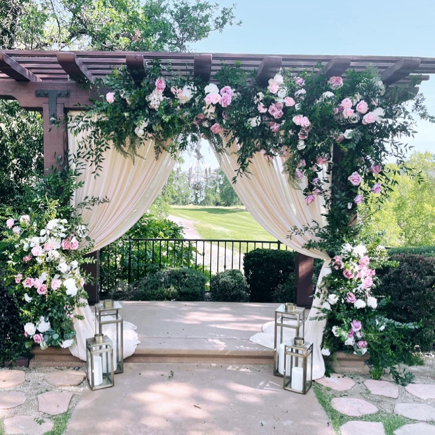 a pergola decorated with pink and white flowers and lanterns