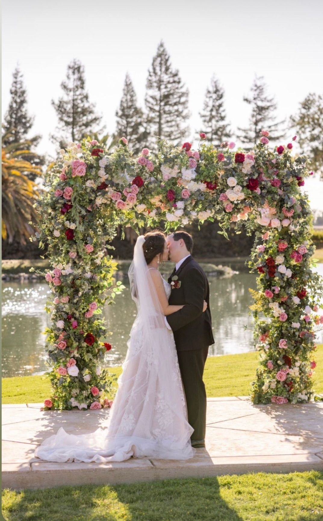 a bride and groom kiss under a floral arch