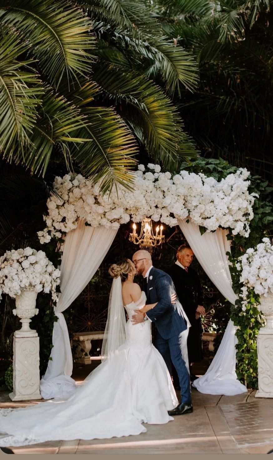 a bride and groom kiss under a white floral arch