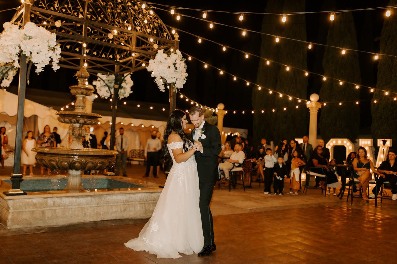 A bride and groom are dancing at their wedding reception in front of a fountain.