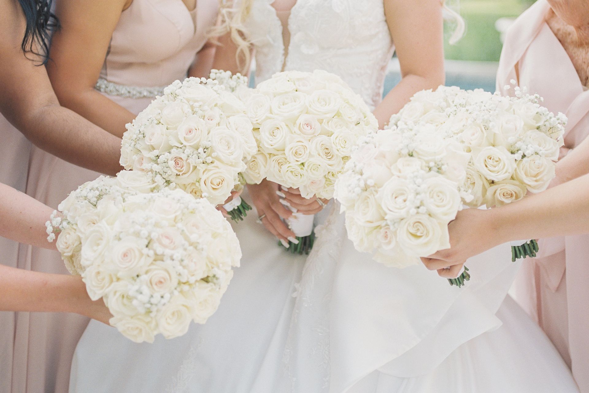 A bride and her bridesmaids are holding white bouquets of flowers.