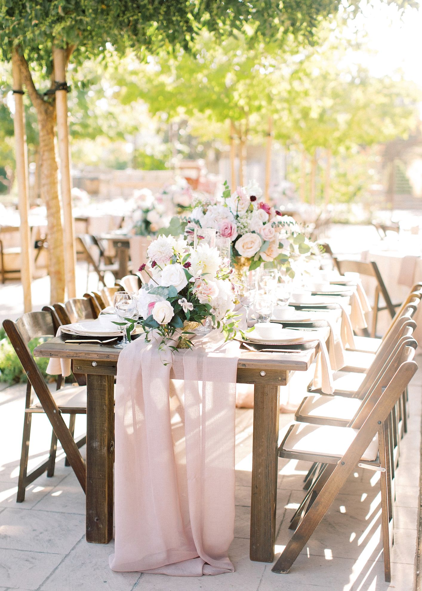 A long wooden table with a pink table runner and flowers on it.