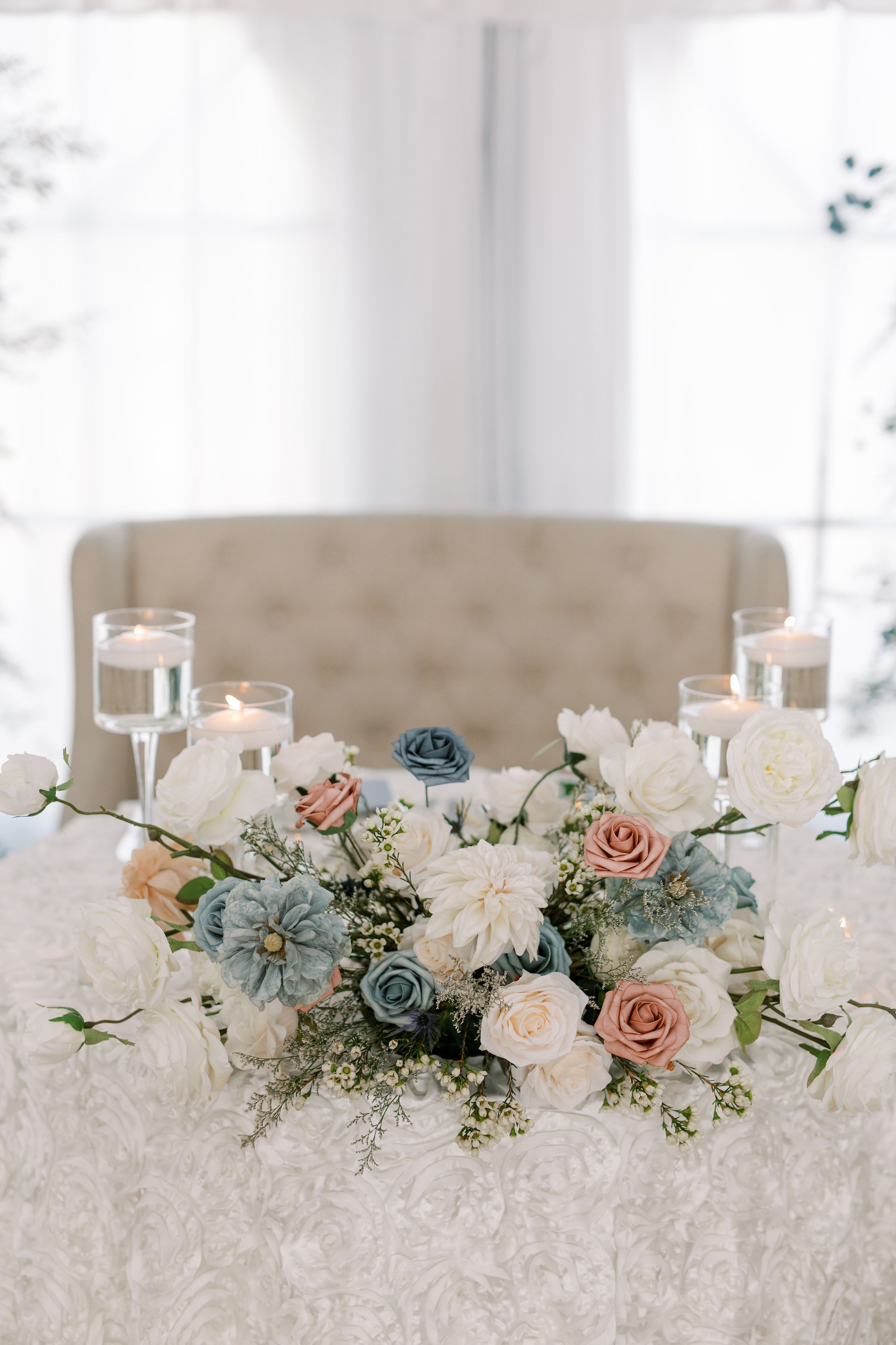 A table with flowers and candles on it and a couch in the background.