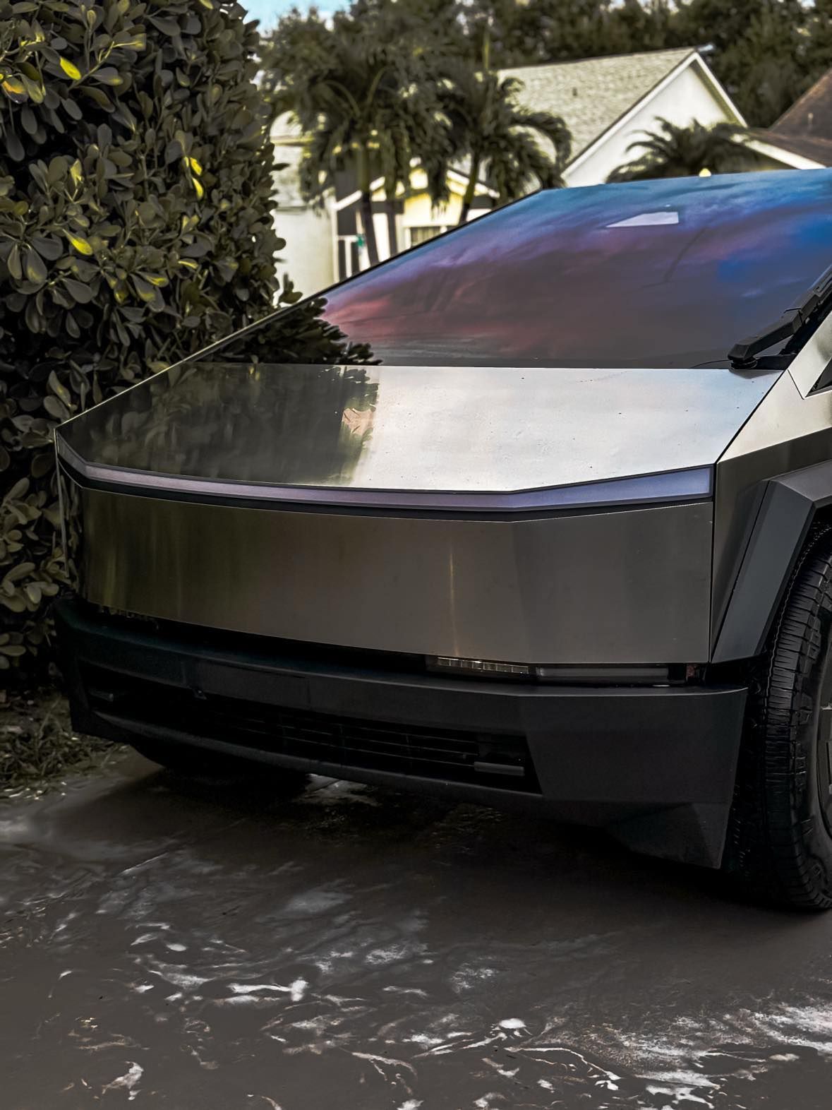 A tesla cybertruck is parked in a driveway in front of a house.
