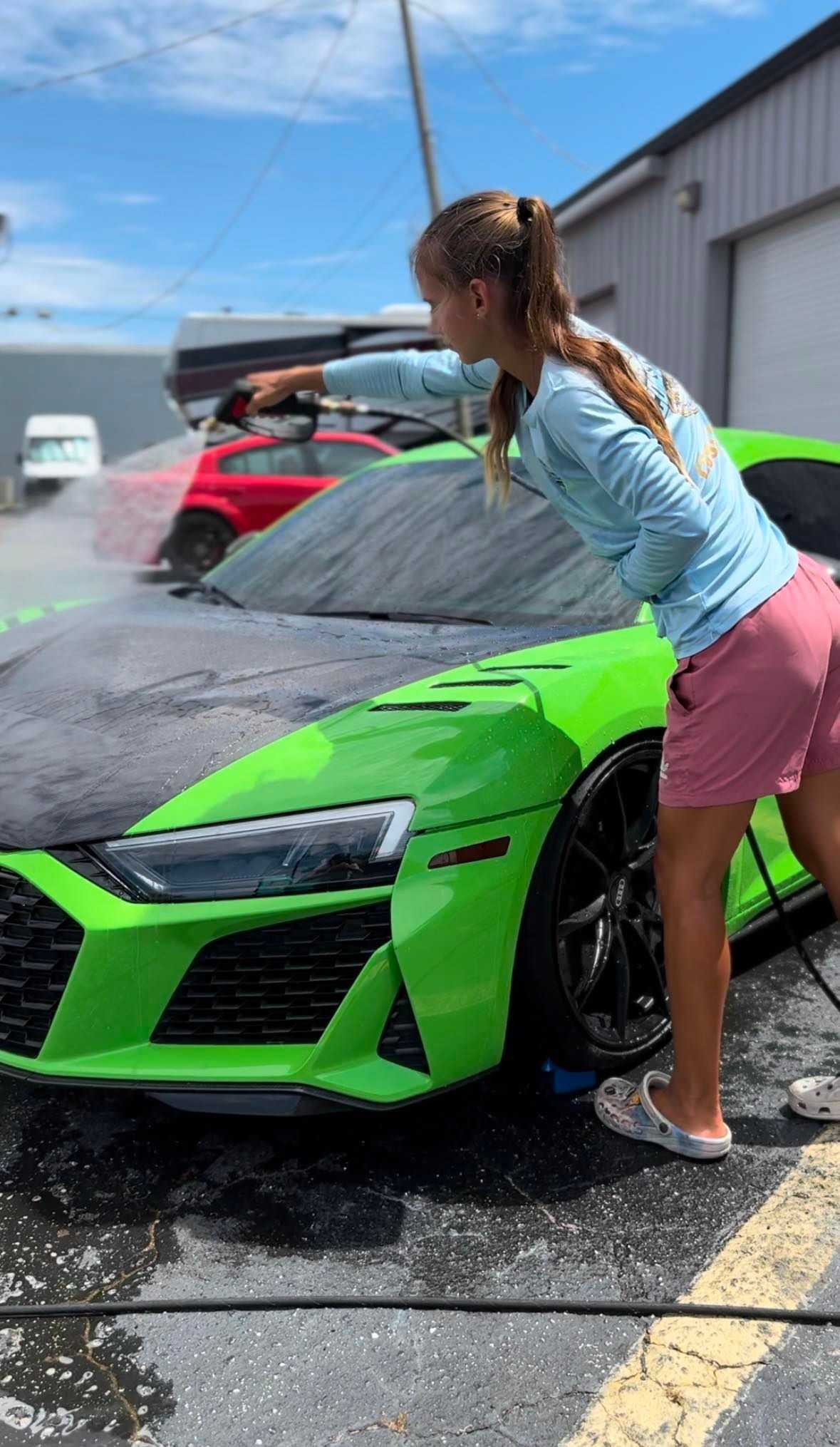 A woman is washing a green sports car in a parking lot.