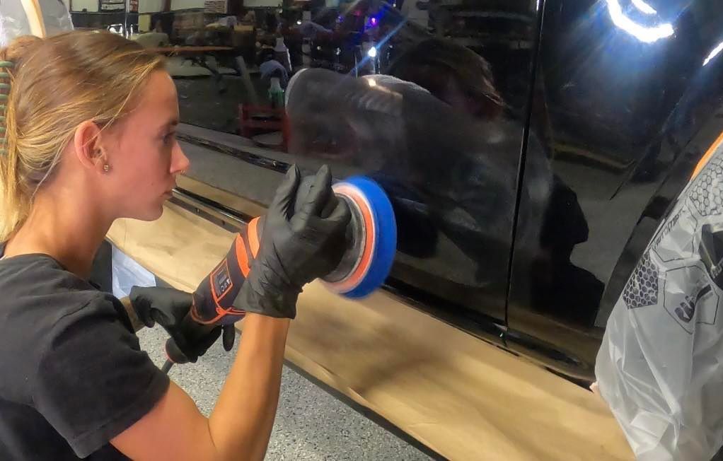 A person is polishing a red car with a machine.