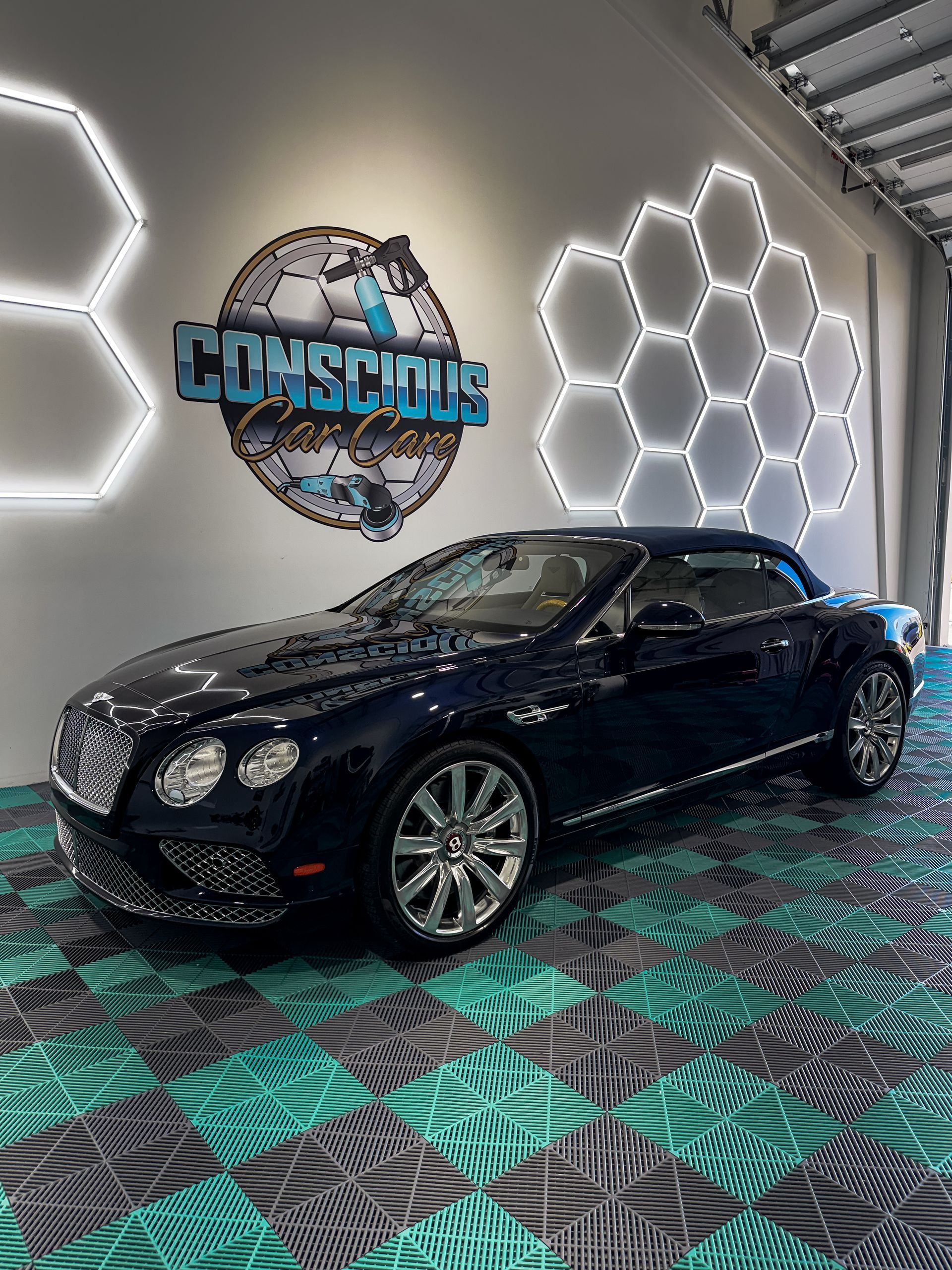 Black luxury sedan in a showroom with LED honeycomb wall lights and a teal-black patterned floor