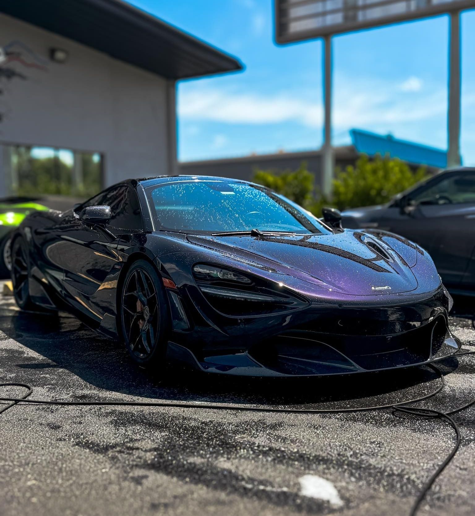 A purple mclaren 720s is parked in a parking lot in front of a building.