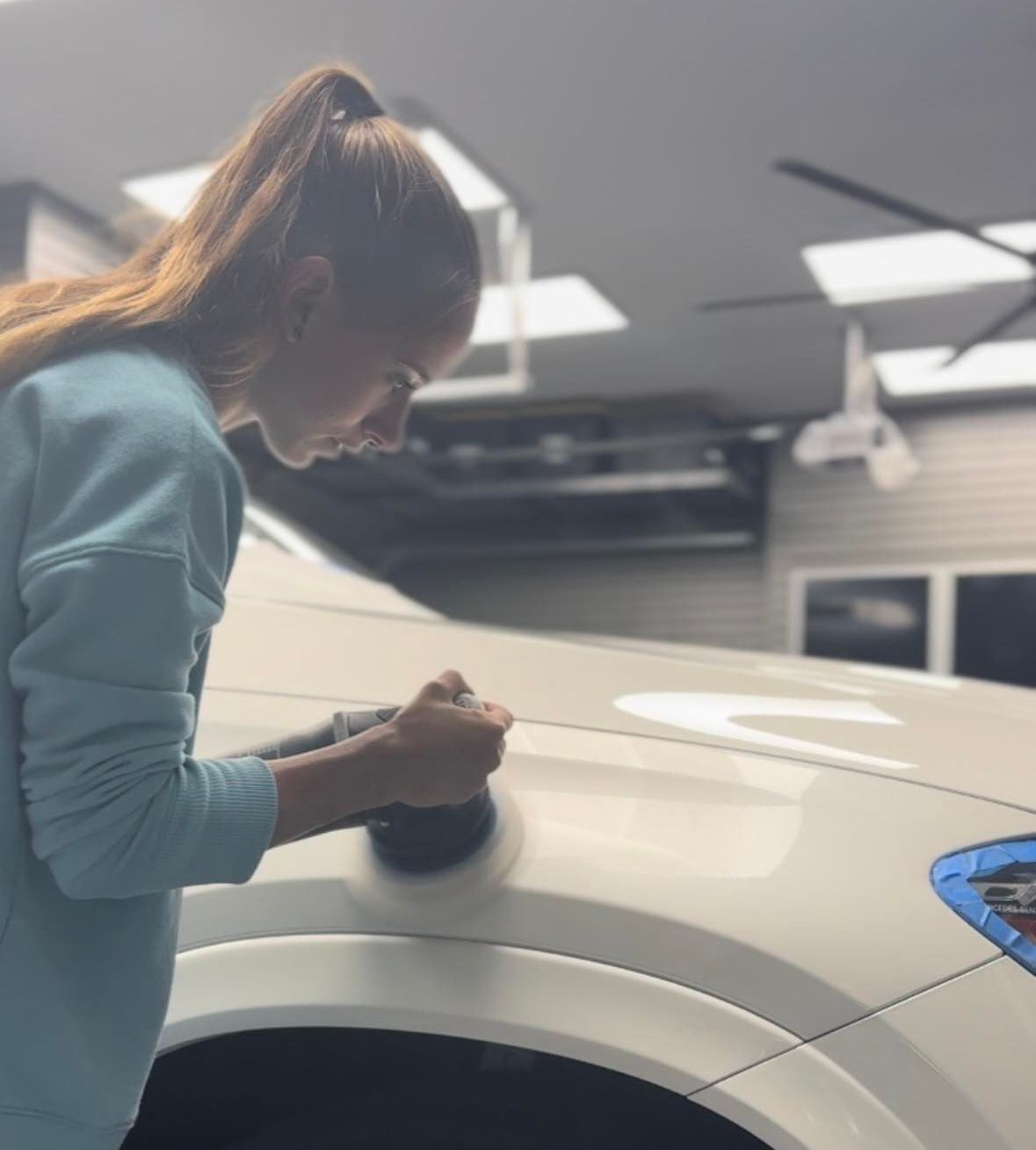 A woman is polishing a car in a garage.
