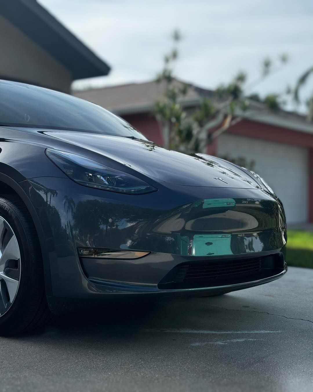 A tesla model 3 is parked in a driveway in front of a house.