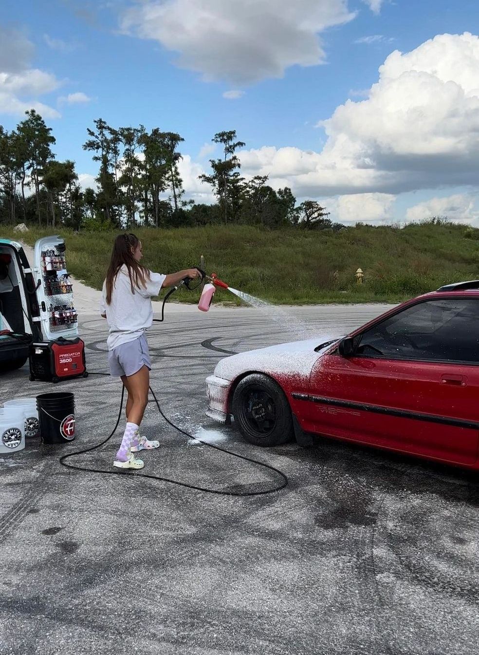 A woman is washing a red car with a hose.