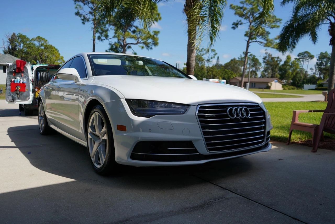 A white audi a7 is parked in a driveway next to a red chair.