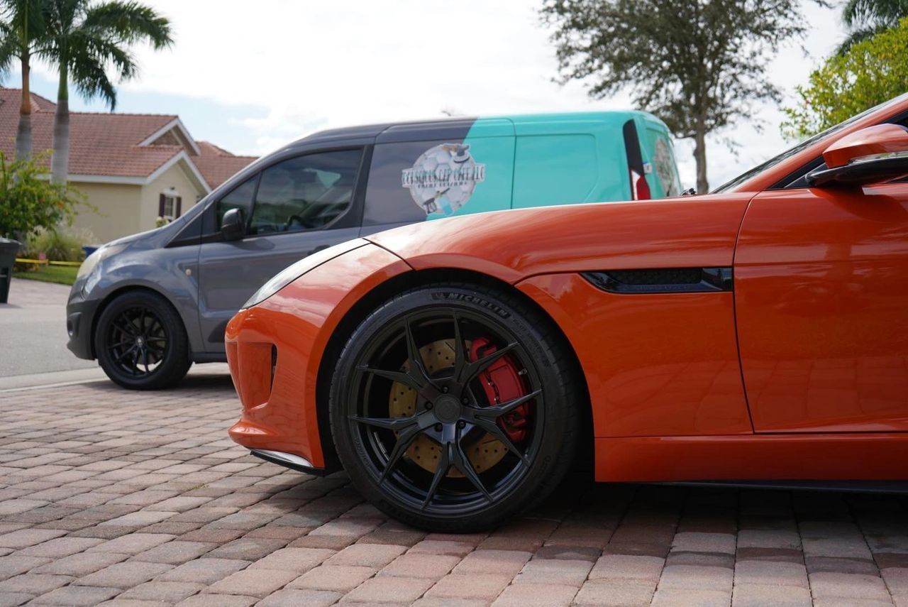 Two cars are parked next to each other on a brick driveway.