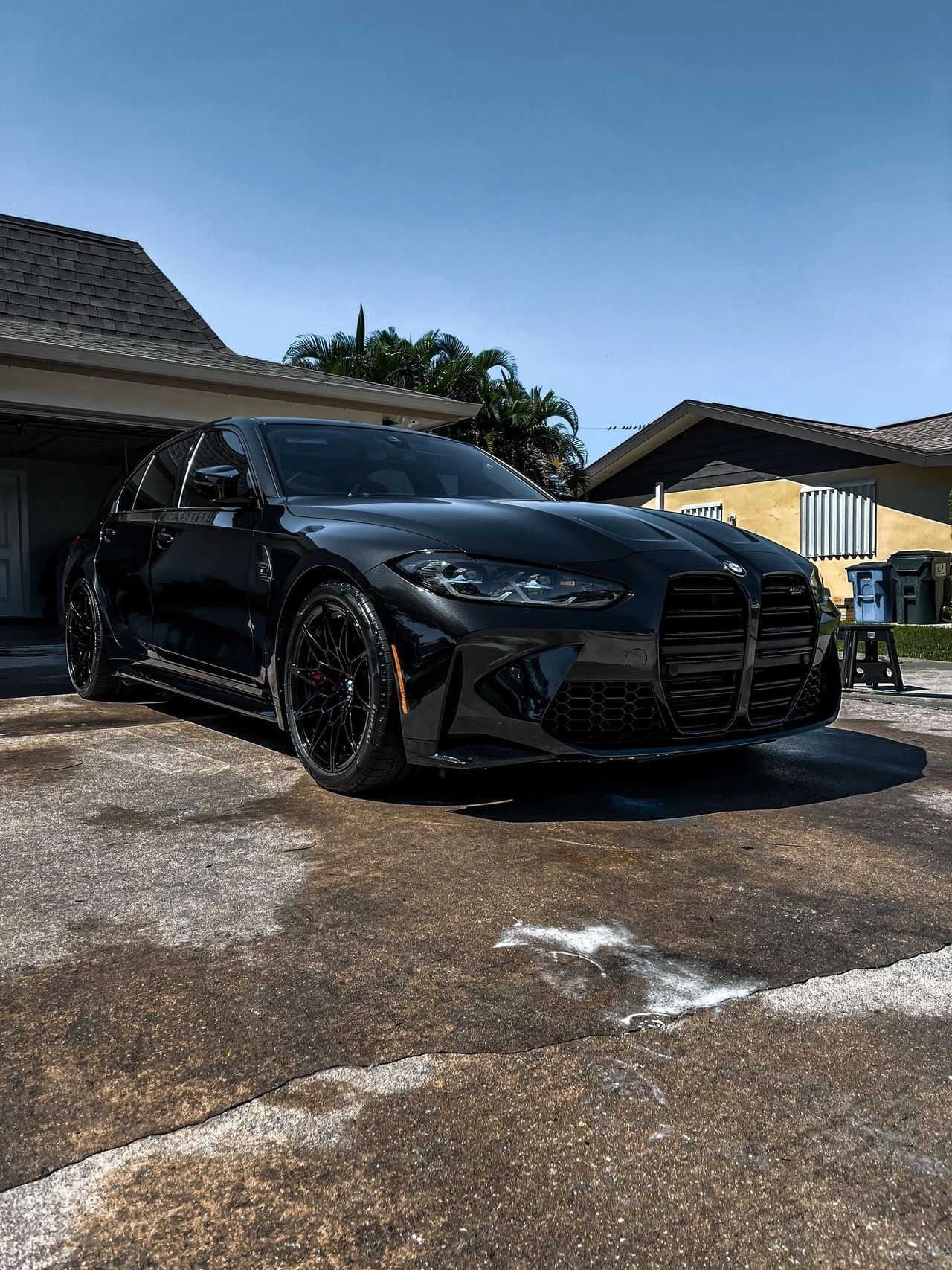 A black bmw m4 is parked in a parking lot in front of a house.