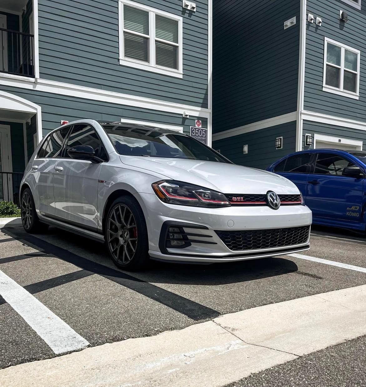 A white car is parked in front of a blue building.