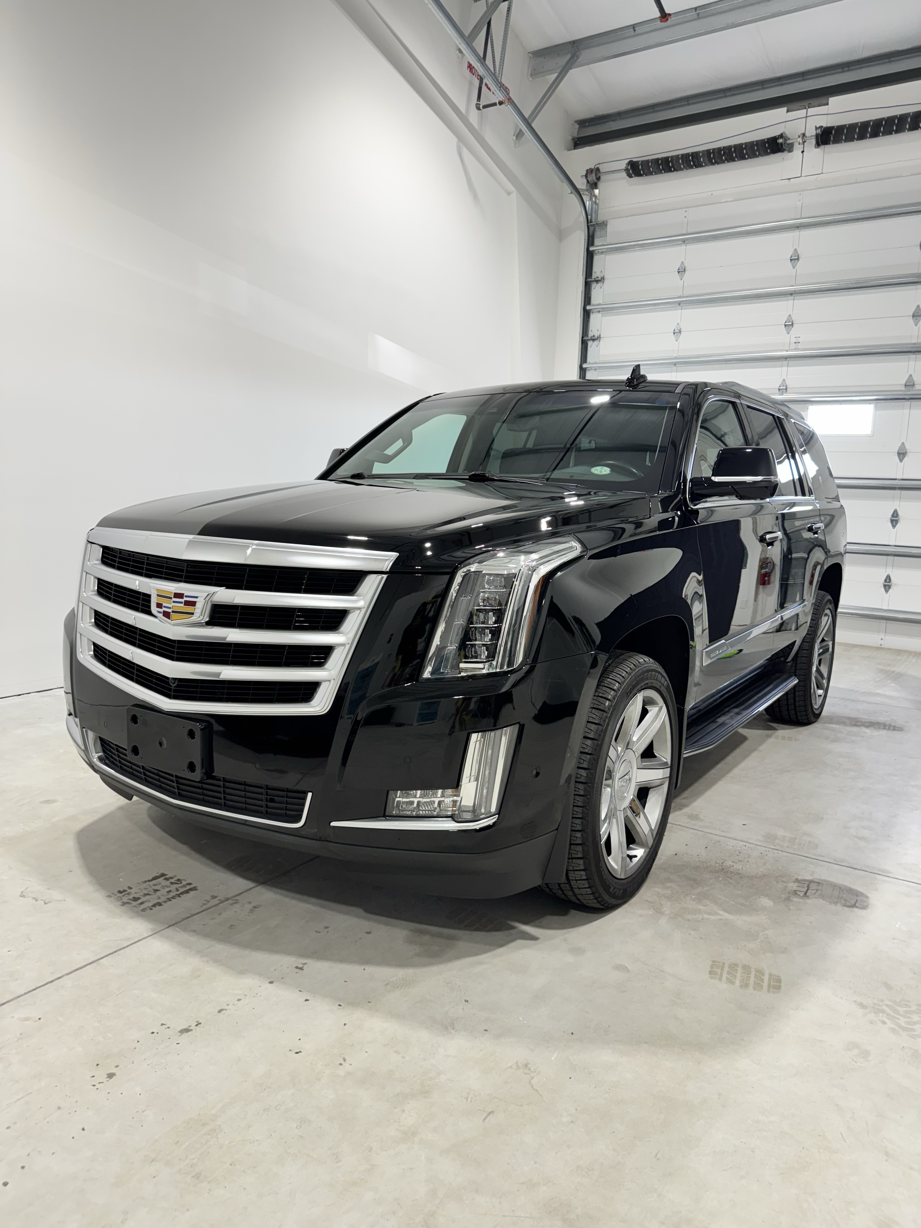 Black Cadillac SUV parked inside a garage, bright lighting.
