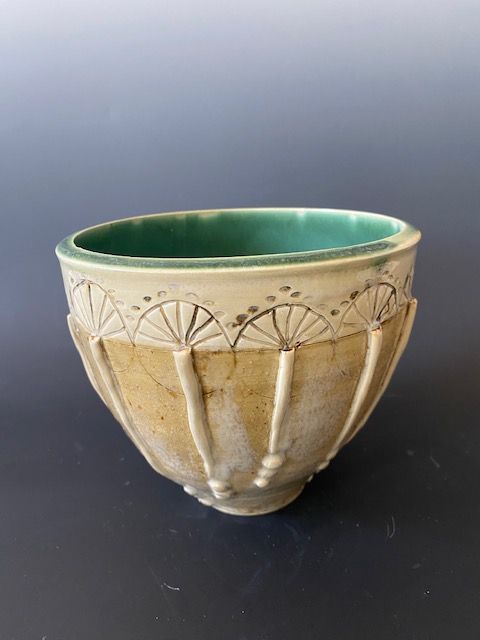 Ceramic bowl with fan-like carvings and a teal interior. Beige exterior, dark background.