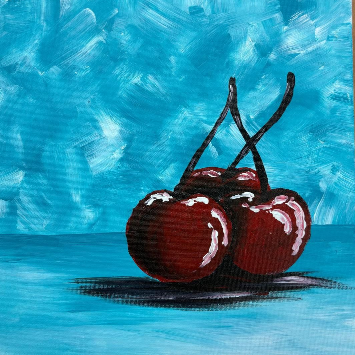 Three cherries with stems, on a light blue surface, against a textured, darker blue background.