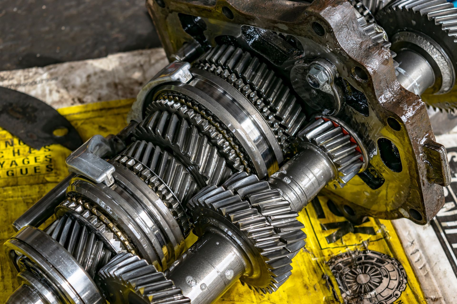 Close-up of a greasy metal gear transmission assembly on a yellow workbench mat