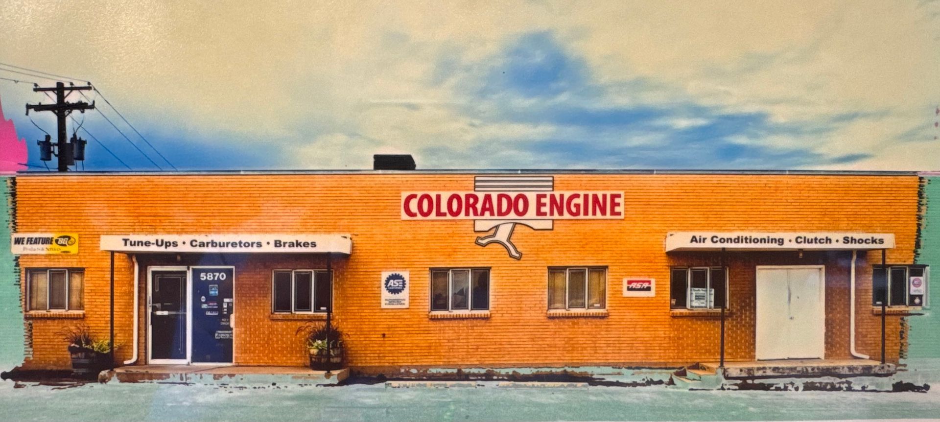 Exterior of Colorado Engine storefront, an orange brick building with bold red signage and parked vehicles | Colorado Engine & Complete Auto Repair