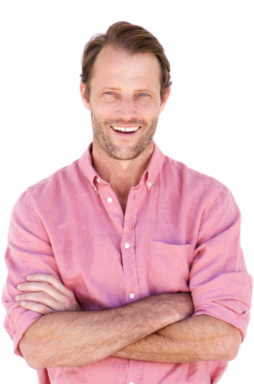 A man in a pink shirt is smiling with his arms crossed
