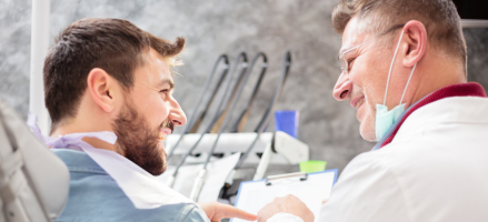 A dentist is talking to a patient in a dental chair about cental crowns.