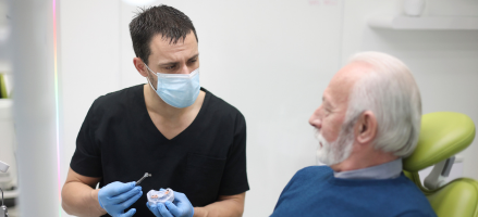 A dentist is talking to an older man in a dental chair about a needed root canal.