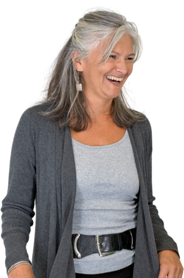 A woman with gray hair is smiling and wearing a grey cardigan