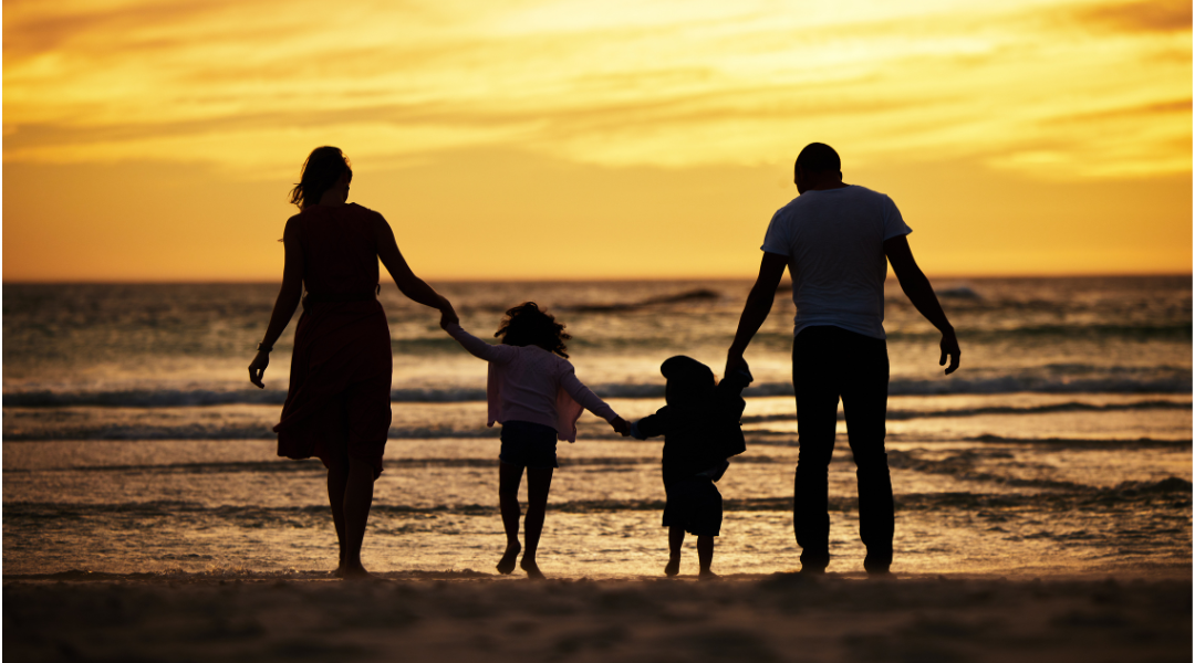 A family is walking on the beach at sunset holding hands.