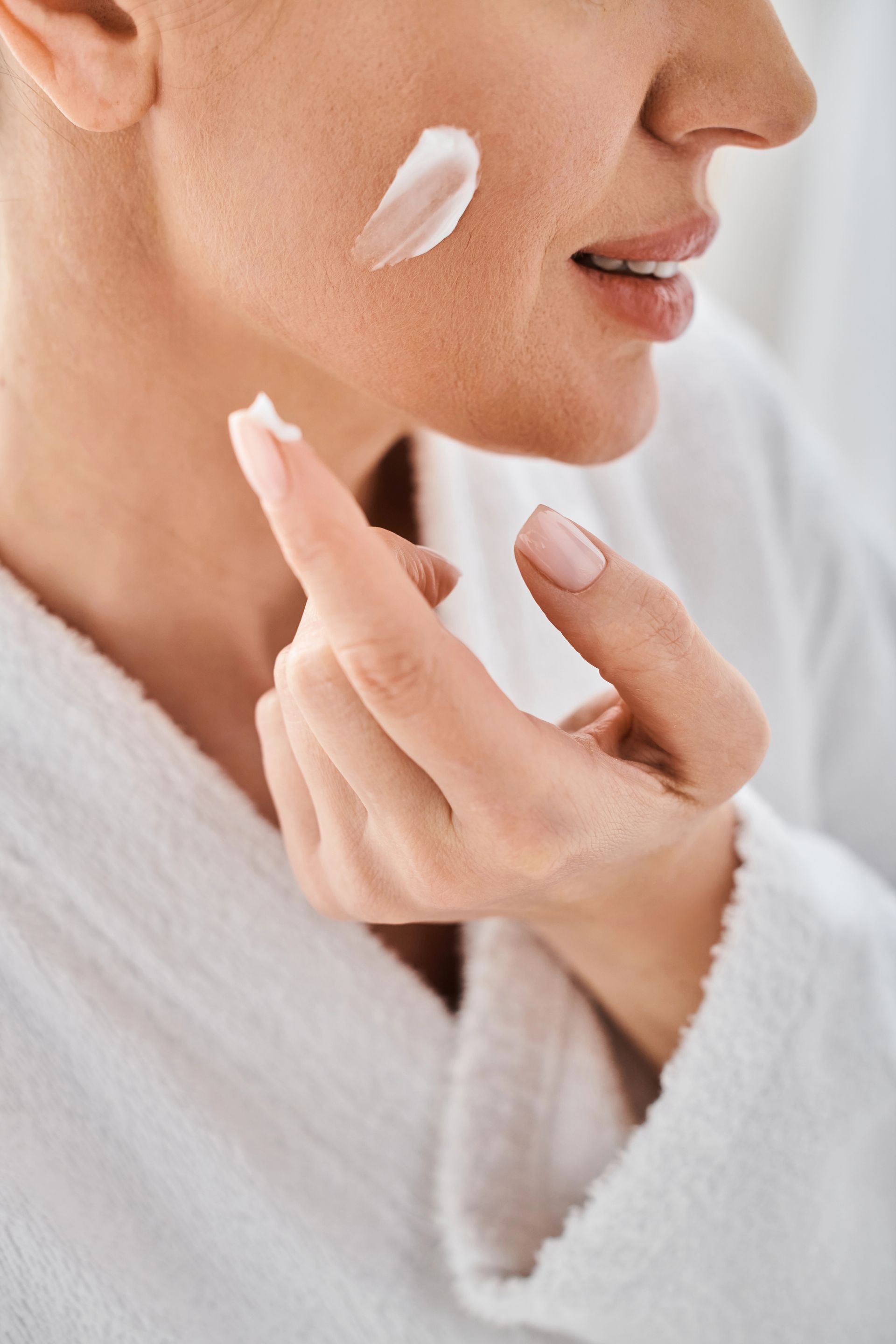Donna che si applica la crema sulla guancia. Primo piano con la crema visibile sulla pelle e sul dito.