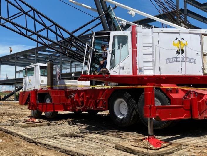 Red industrial crane truck under a steel-framed building in a construction site