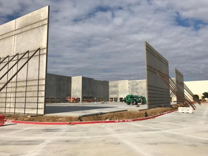 Industrial yard with concrete walls, a red curb, and green construction vehicles under a cloudy sky