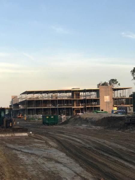 Construction site with a multi-story building under construction beside a muddy dirt road at dusk