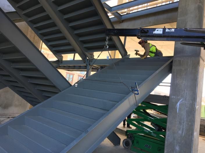Worker installing a large metal staircase in a construction site under an elevated structure