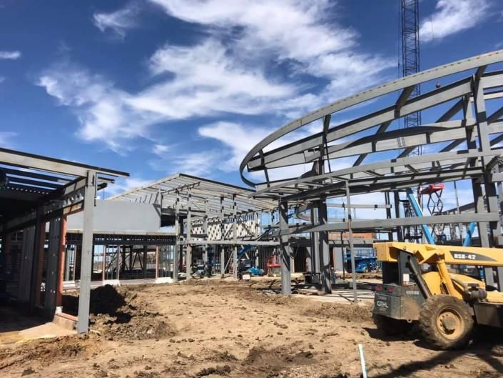 Construction site with steel building frame, dirt ground, and a yellow front loader under a blue sky